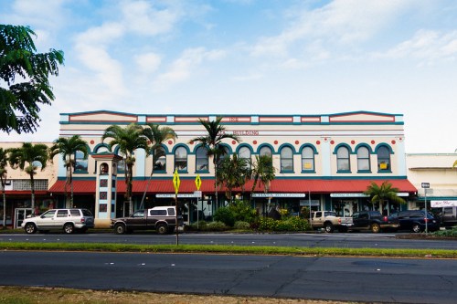 Historic building with colorful arches, palm trees, and parked cars along a street under a blue sky.