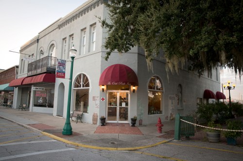 A charming corner building with a red awning, featuring large windows and a welcoming entrance, surrounded by trees.