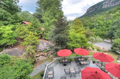 A scenic outdoor patio with red umbrellas, surrounded by lush greenery and mountains in the background.