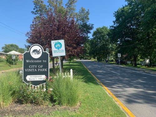A sign welcoming visitors to Vinita Park, with a clear blue sky and trees lining the road.