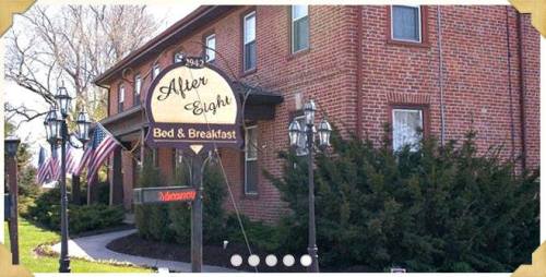 A brick building with a sign reading "After Eight Bed & Breakfast" and American flags, surrounded by greenery.