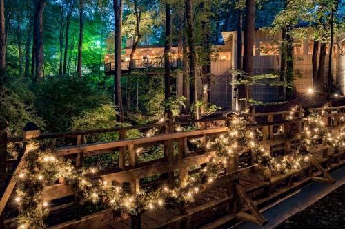A wooden bridge adorned with lights leads to a cozy building surrounded by lush trees at night.