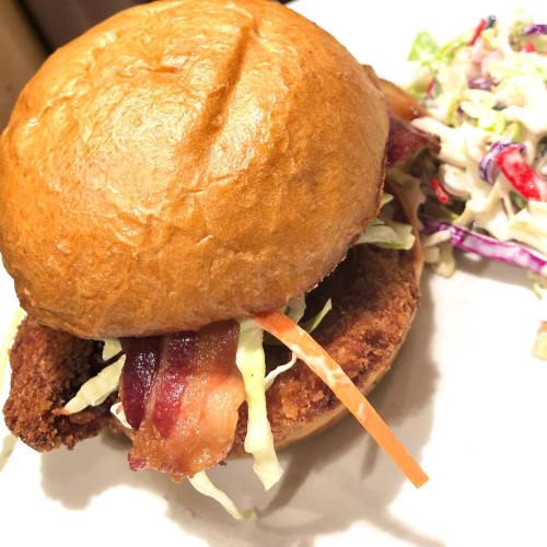 A crispy chicken sandwich with bacon and lettuce on a toasted bun, served with a side of coleslaw.