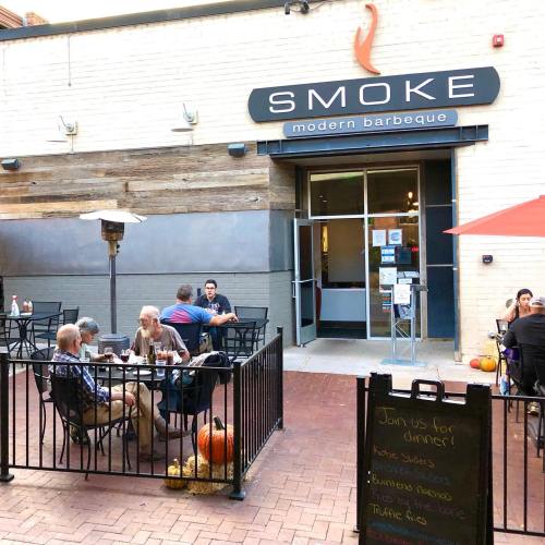 Outdoor dining area of Smoke Modern Barbeque, featuring patrons at tables and a welcoming entrance.