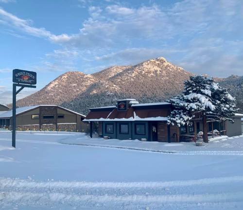 A snowy landscape featuring a rustic building with a sign, surrounded by mountains under a blue sky.