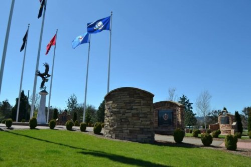A memorial park featuring flags, a stone monument, and a statue of an eagle against a clear blue sky.