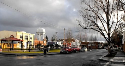 A quiet street scene with a water tower, parked cars, and overcast skies in a small town.