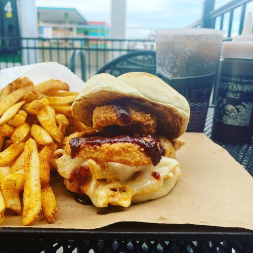 A sandwich with crispy chicken, melted cheese, and barbecue sauce, served with a side of seasoned fries.