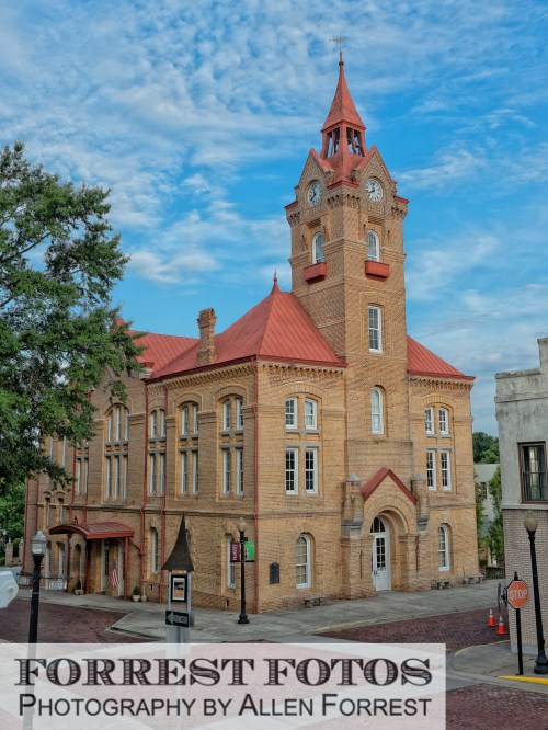 Historic brick building with a clock tower and red roof, set against a blue sky with scattered clouds.