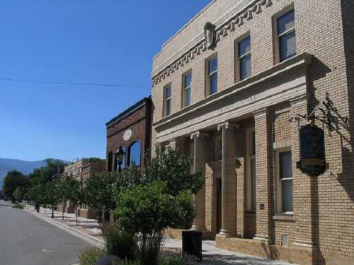 Historic brick buildings line a quiet street under a clear blue sky, with trees and greenery in the foreground.