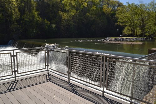 A scenic view of a waterfall cascading over a dam, surrounded by lush greenery and a calm river.