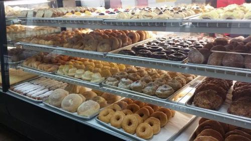 A display case filled with a variety of baked goods, including donuts, pastries, and cookies on multiple shelves.