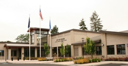 Modern city building with flags, surrounded by greenery and landscaping, labeled "City of Keizer."