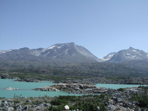 A scenic view of mountains with snow caps, surrounded by turquoise lakes and rocky terrain under a clear blue sky.