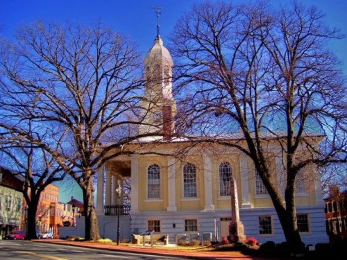 Historic building with a clock tower, surrounded by bare trees against a clear blue sky.
