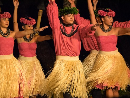A group of dancers in traditional Hawaiian attire perform a hula dance, wearing floral crowns and grass skirts.