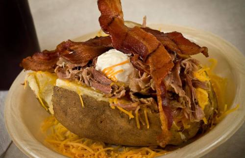 A loaded baked potato topped with shredded meat, cheese, a dollop of sour cream, and crispy bacon.