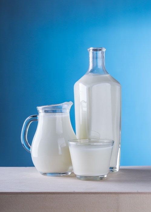 Three glass containers of milk: a pitcher, a bottle, and a small glass, set against a blue background.