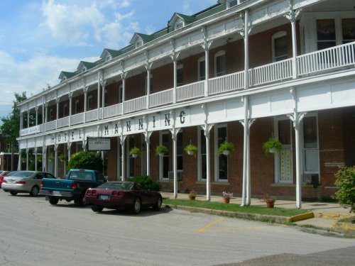 Historic hotel with a white porch, green roof, and parked cars in front under a blue sky with scattered clouds.