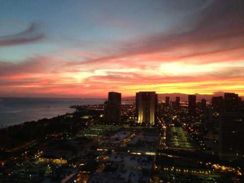 A vibrant sunset over a city skyline, with colorful clouds and lights reflecting on the water.