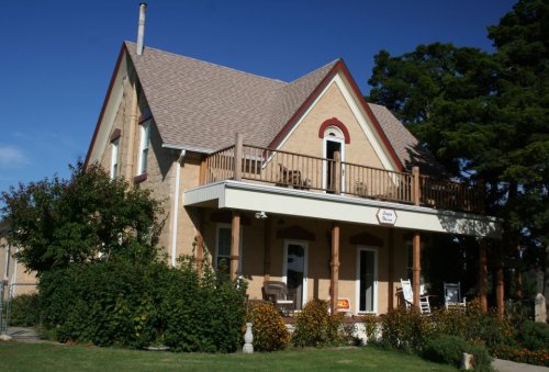 A charming two-story house with a porch, surrounded by greenery and under a clear blue sky.