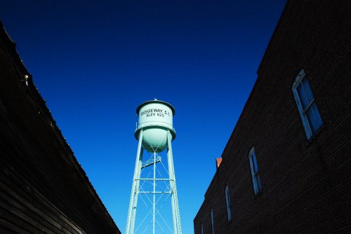 A green water tower stands between two buildings against a clear blue sky.