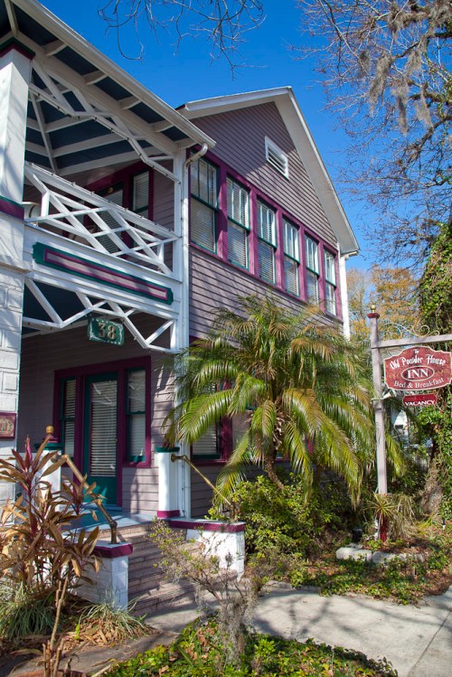 Historic inn with a charming facade, featuring purple accents and lush greenery, set against a clear blue sky.