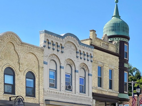 Historic brick buildings with decorative details and a green domed tower against a clear blue sky.