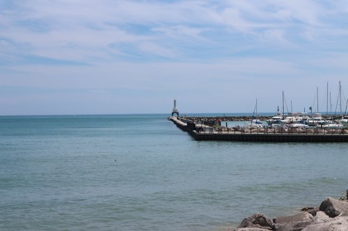 A calm sea with a marina and boats, featuring a pier extending into the water under a blue sky.
