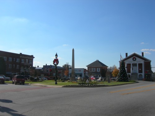 A town square featuring a monument, festive decorations, and buildings under a clear blue sky.