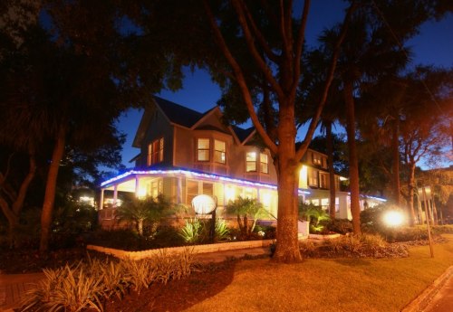 A charming house illuminated with blue lights at night, surrounded by trees and landscaped gardens.