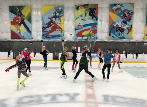 A group of skaters in colorful outfits performs on ice, surrounded by vibrant murals in an indoor rink.