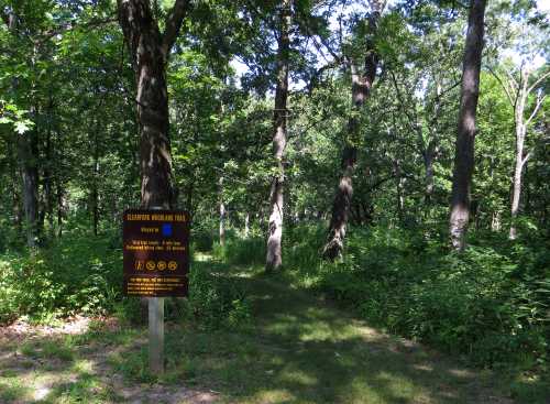 A wooded trail entrance with a sign for Cleaforn Mountain Trail, surrounded by lush greenery and tall trees.