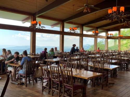 A spacious restaurant with wooden tables and chairs, large windows showcasing mountain views, and diners enjoying their meals.