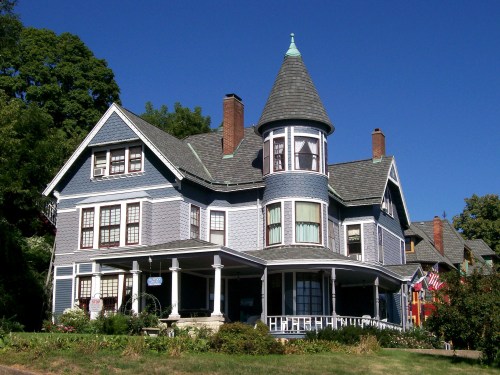 A large, colorful Victorian house with a turret, porch, and blue siding against a clear blue sky.