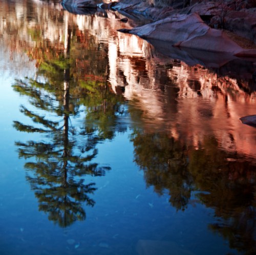 A serene lake reflects trees and rocky shores, creating a tranquil natural scene.