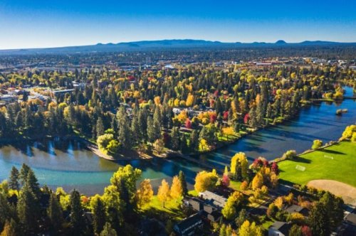 Aerial view of a vibrant landscape with rivers, trees in autumn colors, and a city in the background under a clear blue sky.