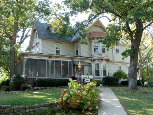 A charming Victorian-style house with a wraparound porch, surrounded by trees and a well-kept garden.