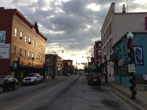A quiet street scene with buildings on either side, under a cloudy sky, decorated for the holiday season.