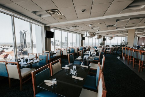 A modern restaurant interior with large windows, tables set for dining, and a view of the city skyline.