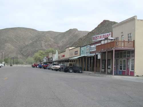 A quiet street lined with small shops and a restaurant, set against a backdrop of mountains.