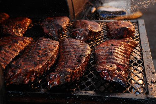Grilled ribs glistening with sauce, sizzling on a barbecue grill with smoke and droplets of water.