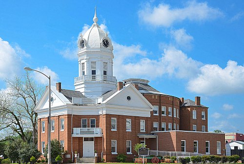Historic brick building with a white dome and clock tower, set against a blue sky with fluffy clouds.