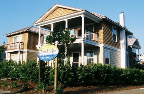 A two-story beach house with a sign reading "Beach Spa" and lush greenery in front. Clear blue sky above.