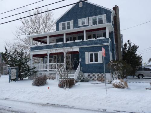 A blue house with multiple balconies, surrounded by snow and bare trees, on a winter day.