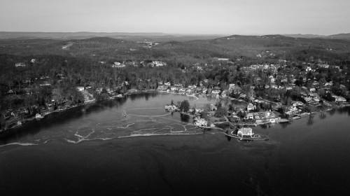 Aerial view of a serene lakeside community surrounded by trees, captured in black and white.