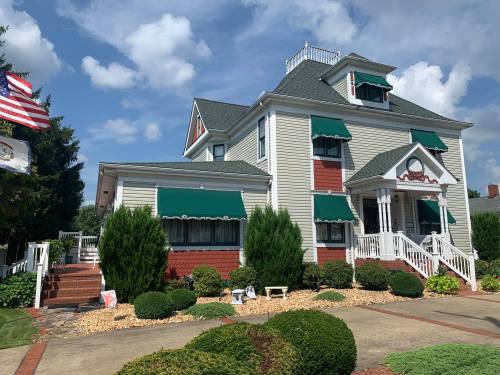 A large, two-story house with green awnings, a porch, and landscaped gardens under a blue sky with clouds.