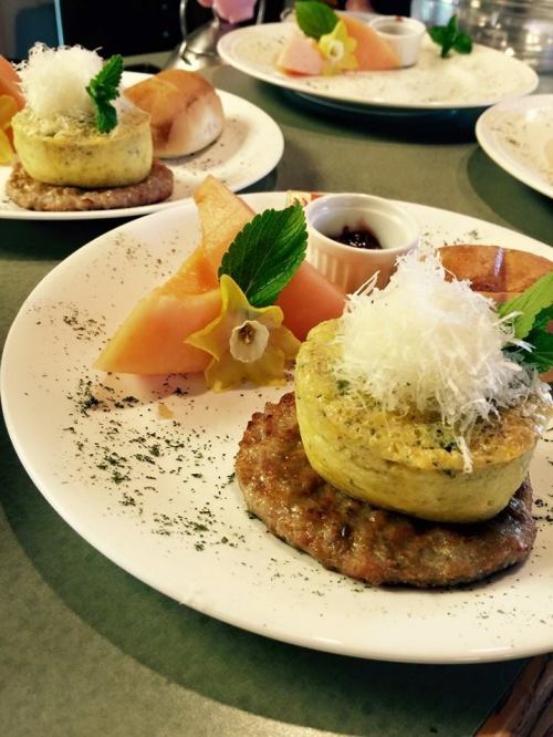 A plate featuring a savory dish with a round egg frittata on a sausage patty, garnished with herbs and fruit slices.