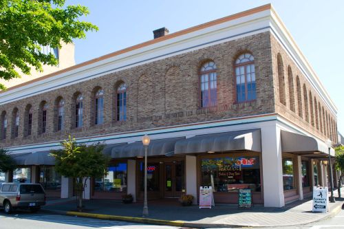 Historic brick building with arched windows, featuring a salon and spa, surrounded by trees and parked cars.