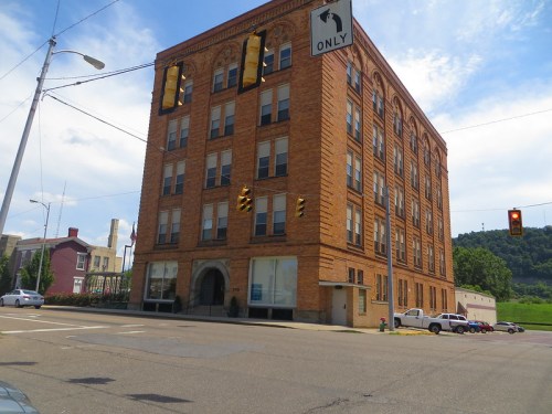 Historic brick building at a street corner with traffic lights and a "One Way" sign under a blue sky.